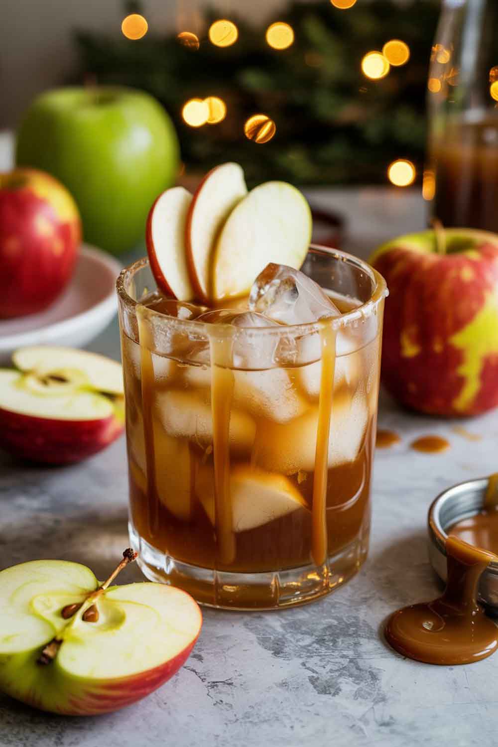 Golden caramel apple mocktail in a rocks glass with ice and apple slices, styled with caramel drizzle and soft Christmas décor.