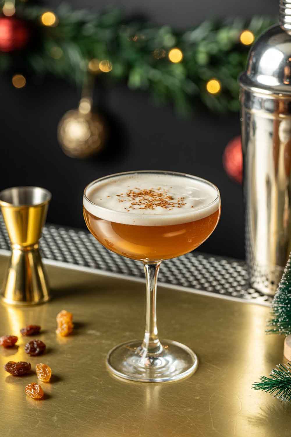 16 Christmas Spiced Rum Cocktails to Sleigh Your Holiday Season 3 A creamy cocktail with a frothy top in a vintage coupe glass, garnished with grated nutmeg. Styled with raisins, a cocktail shaker, and subtle warm lighting on a bar counter with subtle Christmas décor (e.g., garland, ornaments).