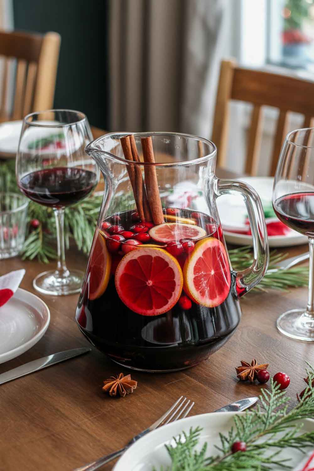 Festive Spiced Rum Sangria A pitcher of red sangria filled with citrus slices, cranberries, and cinnamon sticks. Served with wine glasses on the side. Styled on a wooden dining table set for Christmas brunch, with evergreen sprigs and holiday linens.