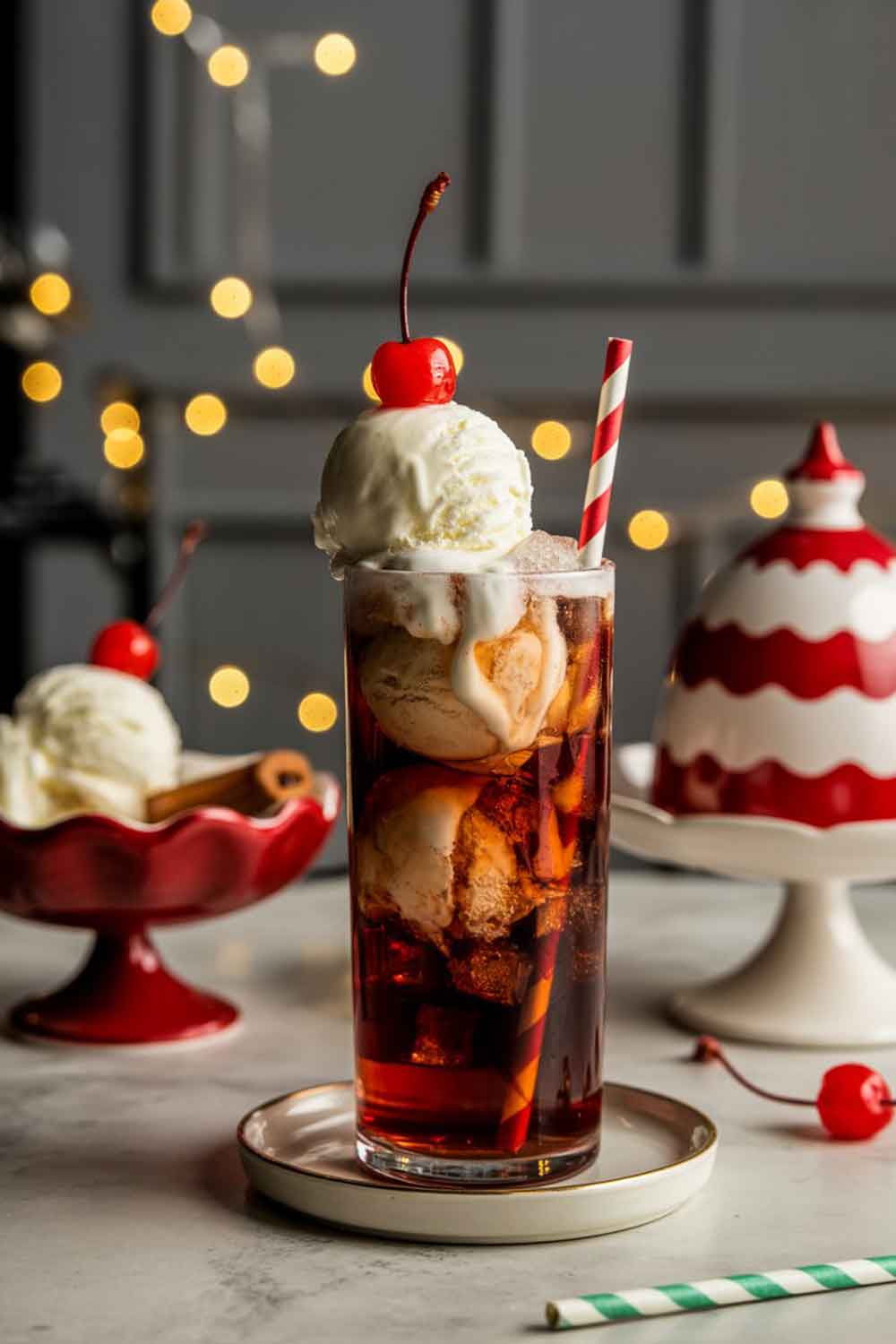 Cherry Vanilla Spiced Rum Float A decadent cocktail float in a tall soda glass with vanilla ice cream floating in cherry soda. Garnished with a maraschino cherry and a red-and-white striped straw. Styled with vintage holiday dessert dishes and soft glowing lights.