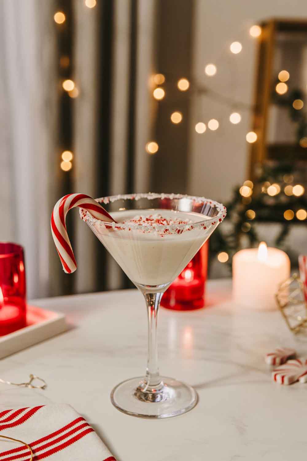 Creamy peppermint martini mocktail in a classic martini glass with crushed candy cane rim, set among red-and-white Christmas décor.