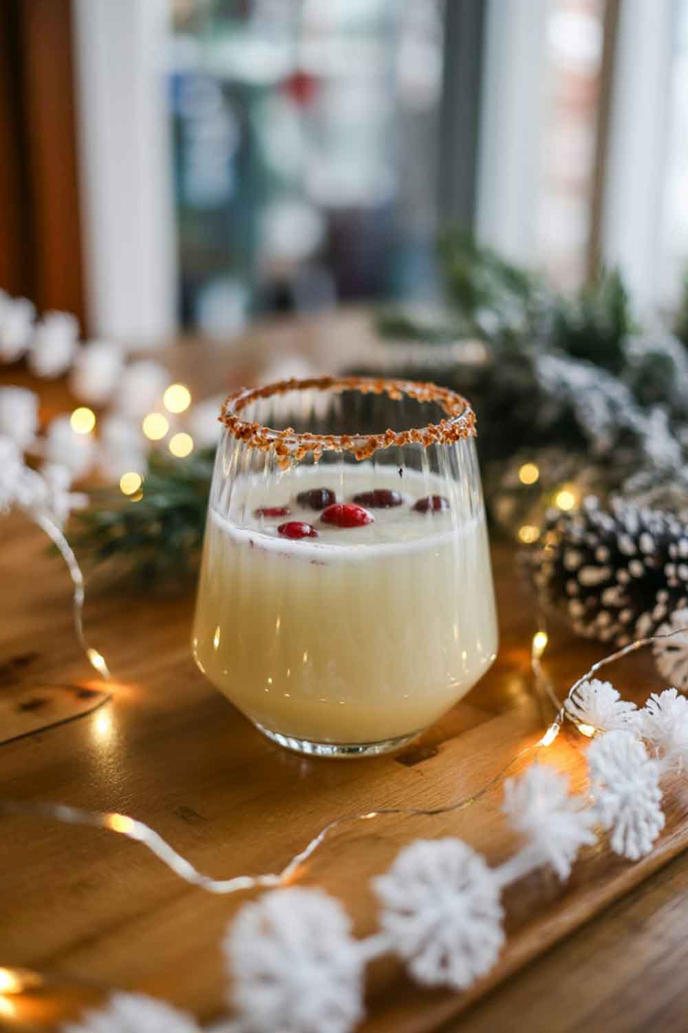 White Christmas Margarita A creamy white margarita in a stemless cocktail glass, rimmed with coconut flakes, garnished with cranberries. Set on a wooden table with white holiday décor, twinkling lights, and soft greenery. Warm indoor lighting for a winter-evening feel.