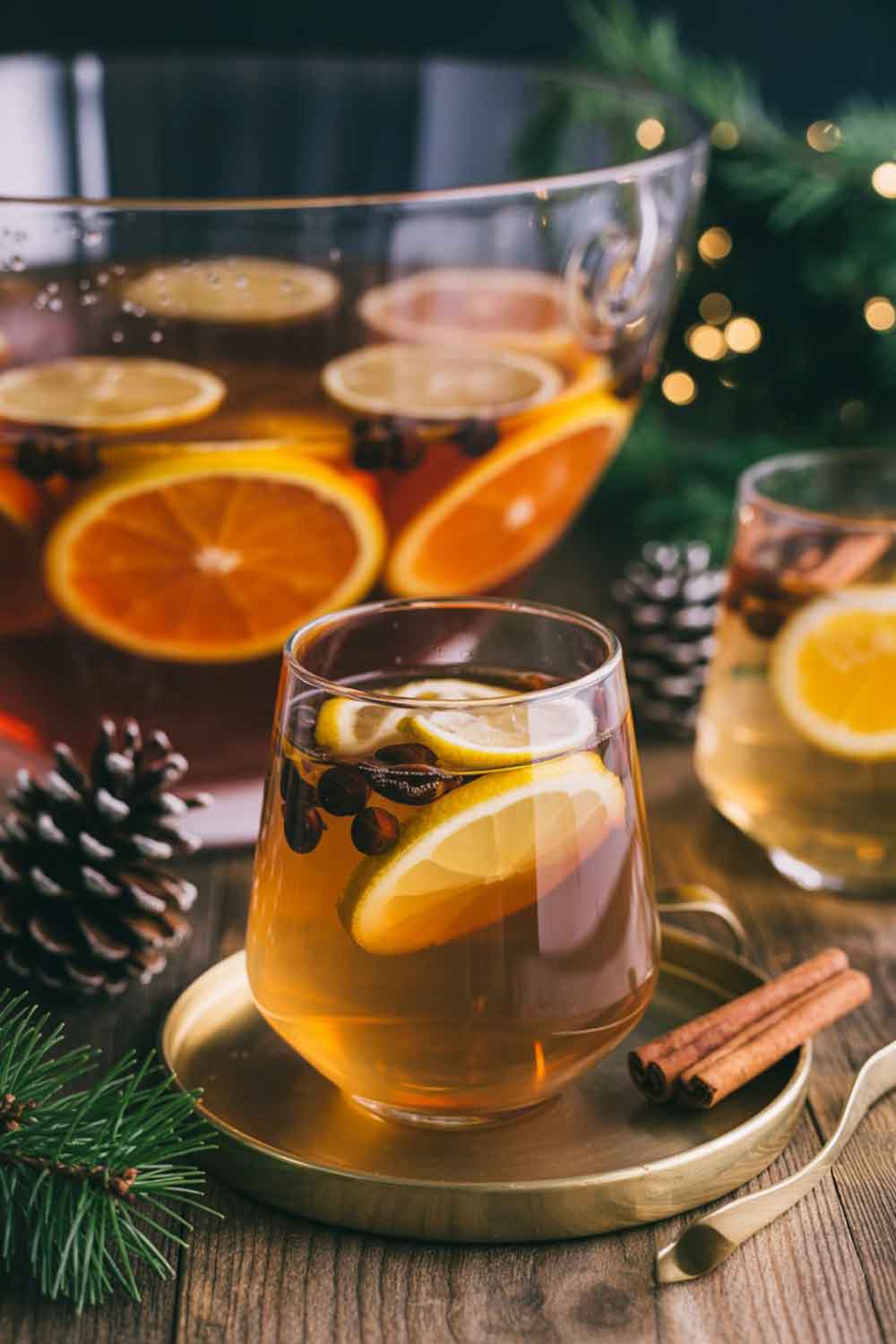 Chai-spiced holiday punch in a clear punch cup with citrus slices, styled beside a punch bowl with festive winter accents.