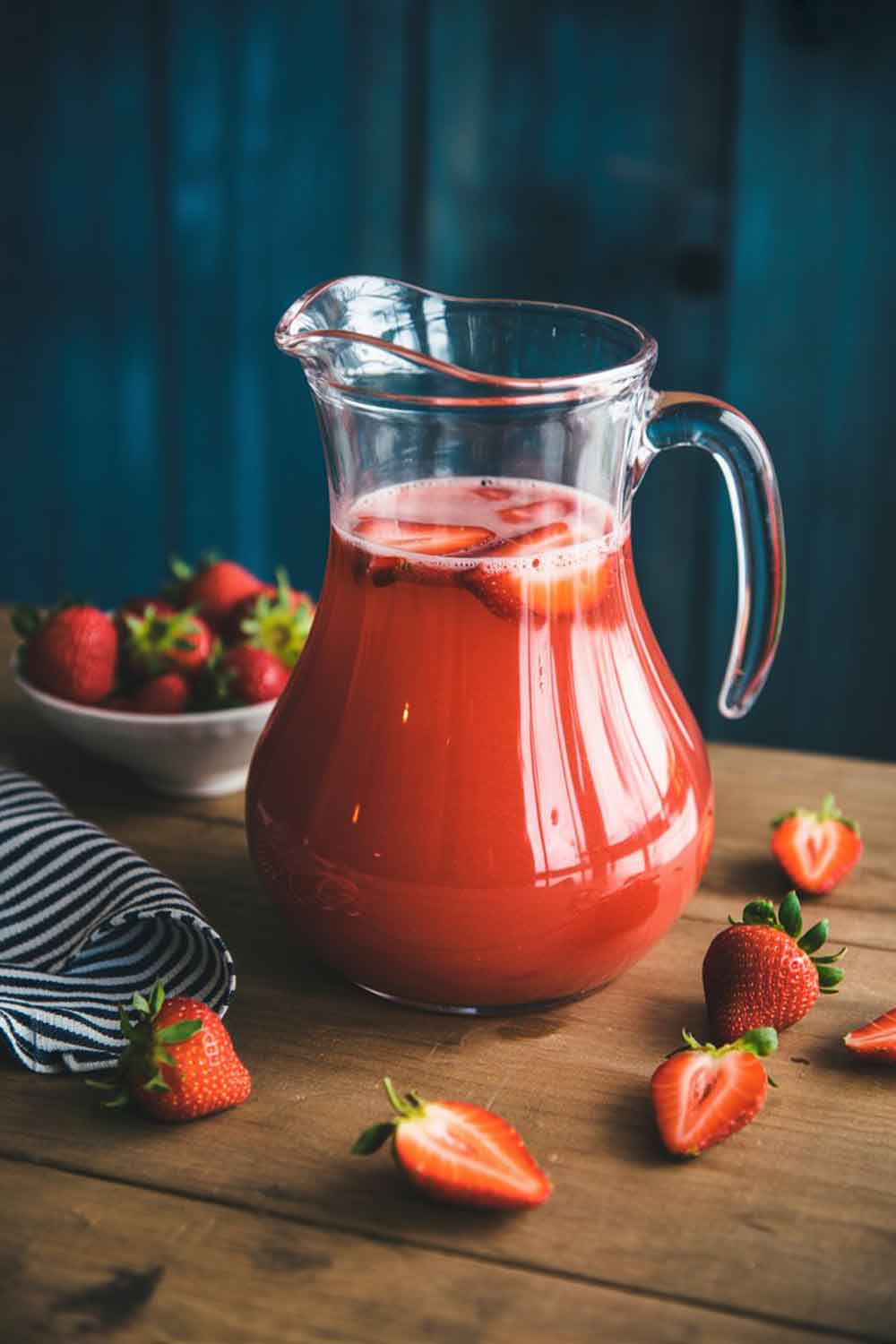 Strawberry Rum Punch Pitcher of refreshing strawberry rum punch with sliced strawberries on a wooden table, a fruity and colourful drink ideal for summer parties.