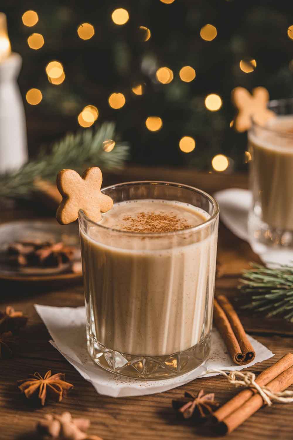Creamy gingerbread mocktail in a rocks glass with nutmeg and a small gingerbread cookie, surrounded by warm Christmas lighting.