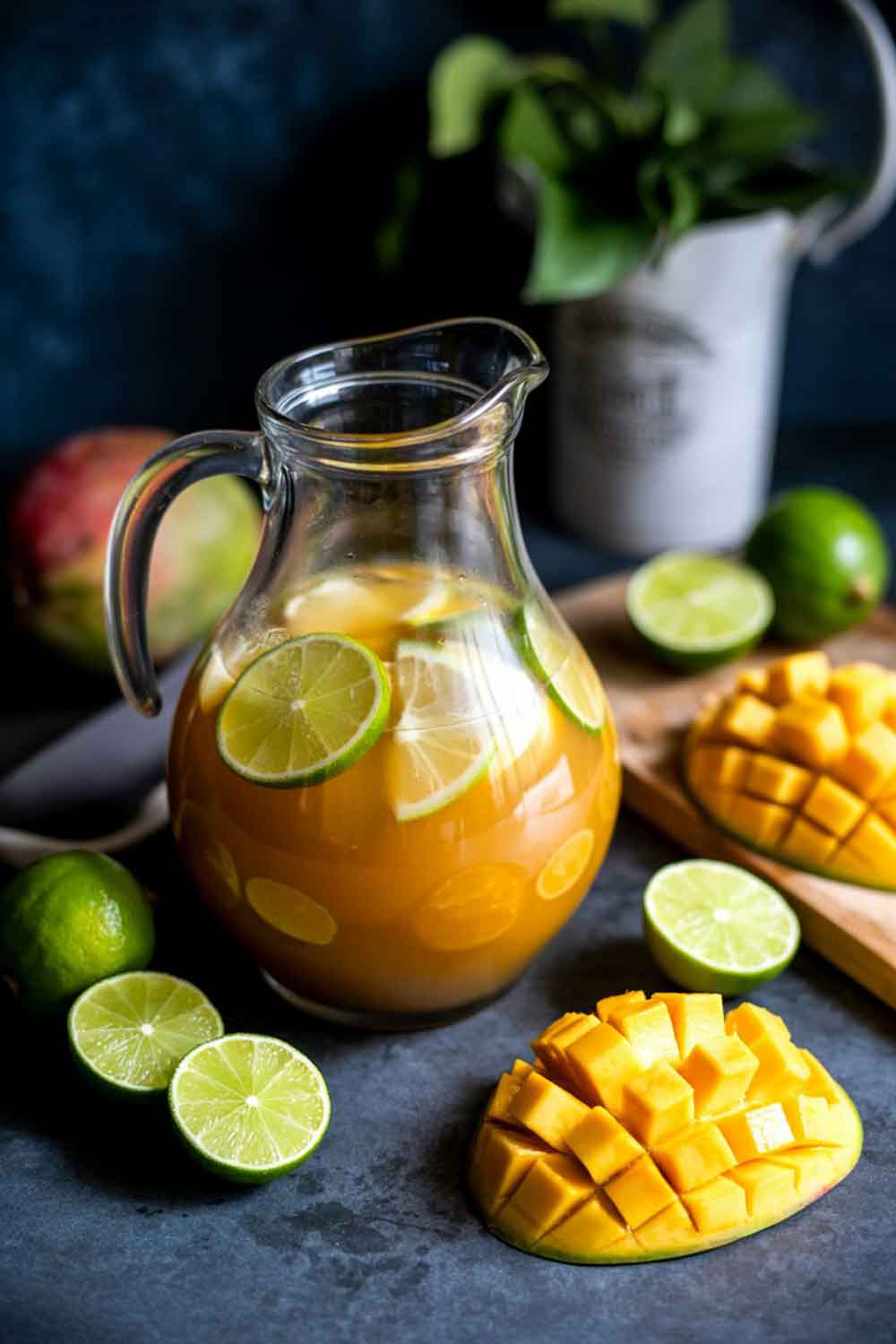 Mango & Lime Rum Punch Jug of mango and lime rum punch surrounded by fresh lime slices and diced mango, a refreshing tropical cocktail perfect for sharing.