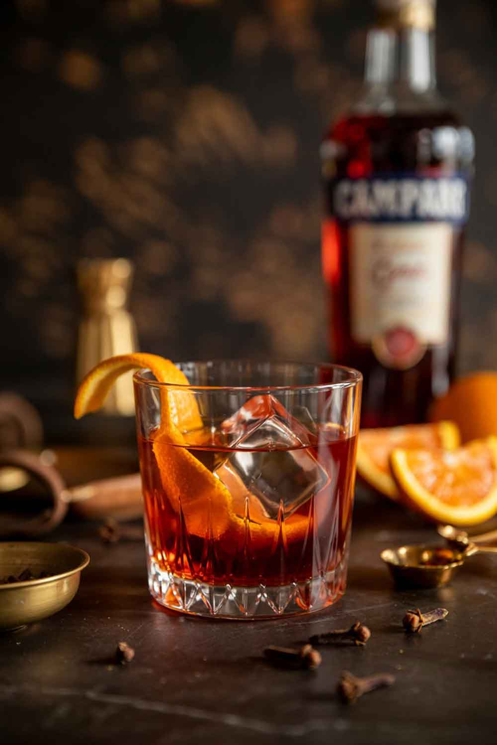 Orange-Spice Negroni Orange-spice Negroni in a crystal rocks glass with toasted orange peel, styled with cloves and warm moody lighting on a wood table.