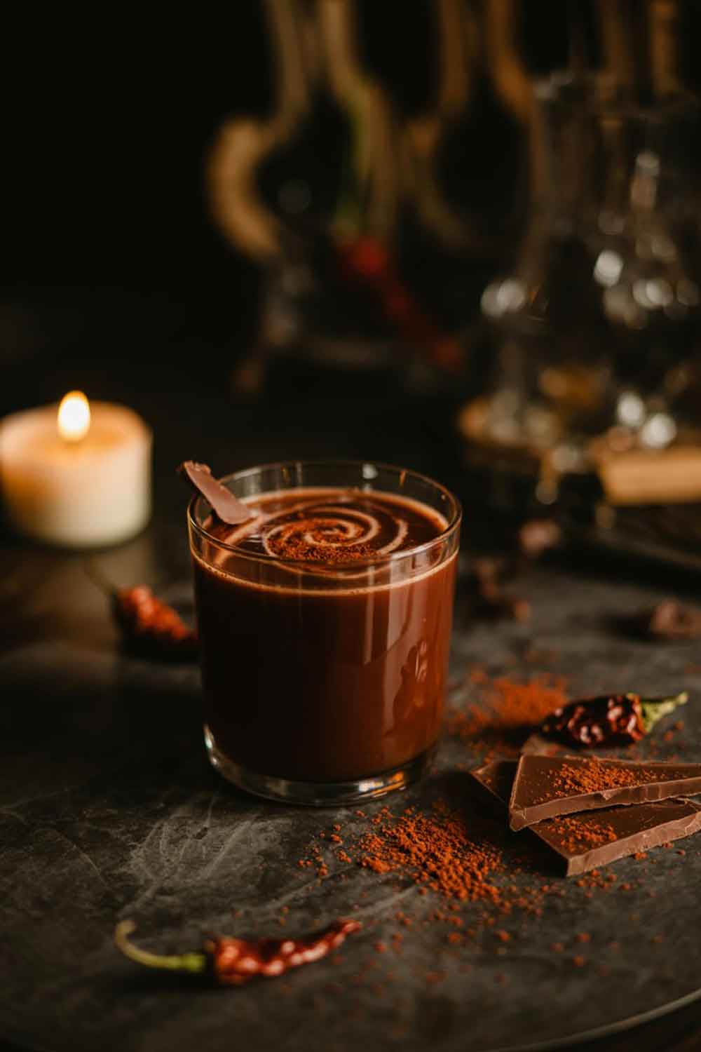 Chilli Chocolate Mezcal Dark chilli chocolate mezcal cocktail with chocolate shavings and chilli powder, styled in a moody home bar setting with candlelight.