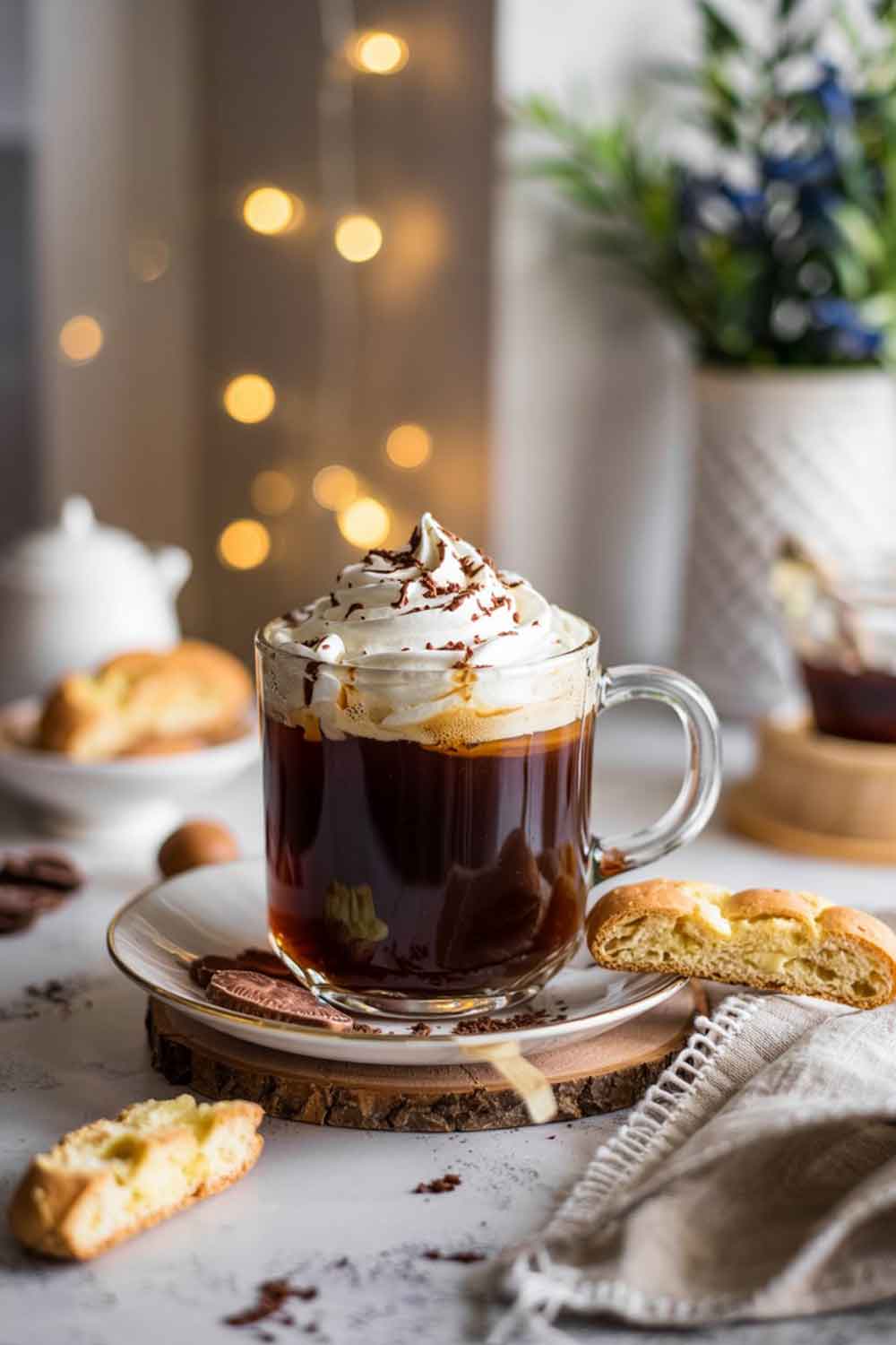 Amaretto Coffee Amaretto coffee in a clear glass mug with whipped cream and chocolate shavings, set beside biscotti in a cozy breakfast nook.