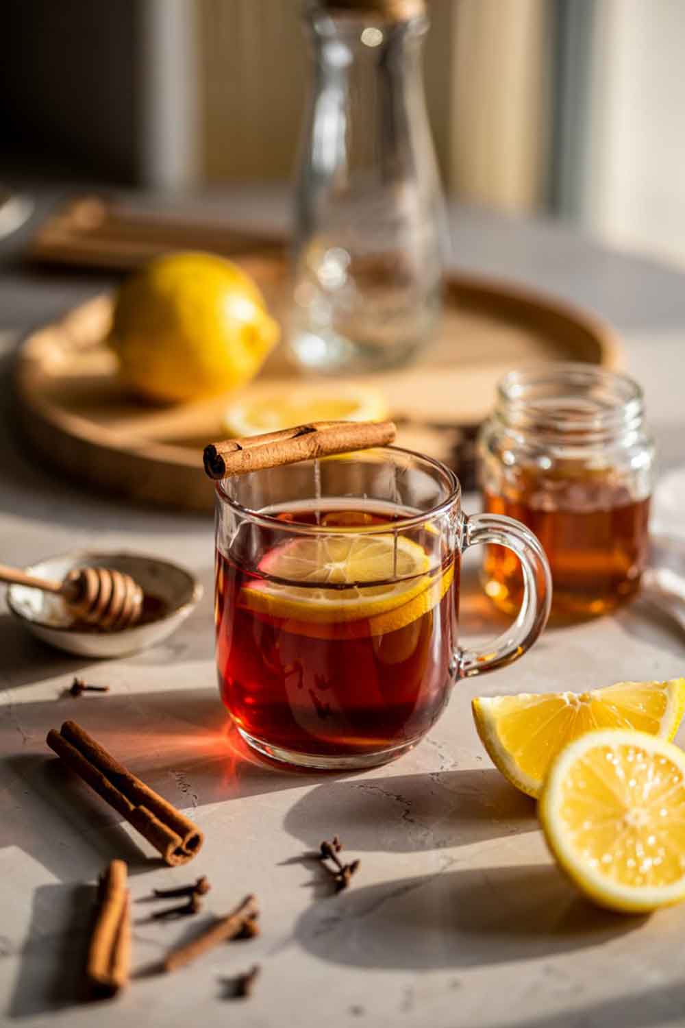 Red Wine Hot Toddy Red wine hot toddy in a ceramic mug with lemon slice and cinnamon, surrounded by cloves, honey, and soft candlelight at home.